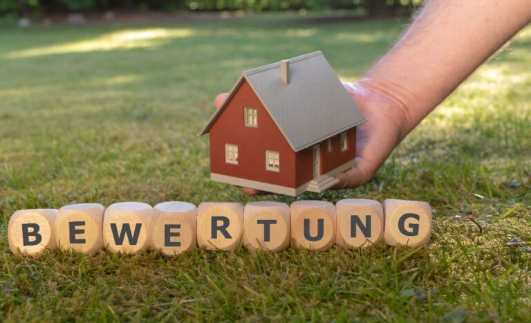 Würfel bilden das Wort "Bewertung" vor einem Modellhaus.